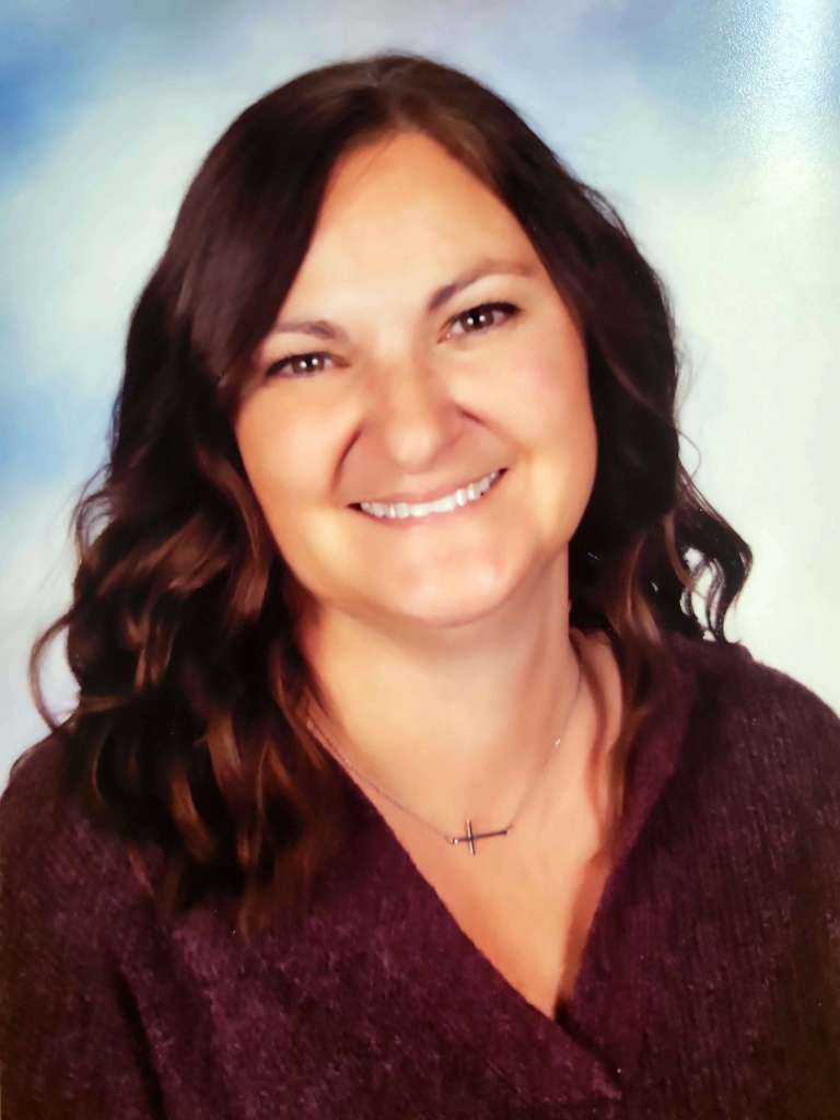 Portrait of Ms. Sherry. Ms. Sherry is a smiling woman with shoulder-length brown hair wearing a purple sweater, set against a blue and white cloud background.